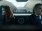 "Two serious people in formal attire sit in the back of a car with a presidential seal, looking out the windows; the environment is tense, with another vehicle visible behind them through the rear window."